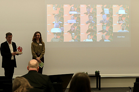 On the left, Dr. Rainer Müssner from BMFTR together with the moderator of the Award Ceremony is standing next to a Zoom call. In the zoom call all 20 awardees are online.